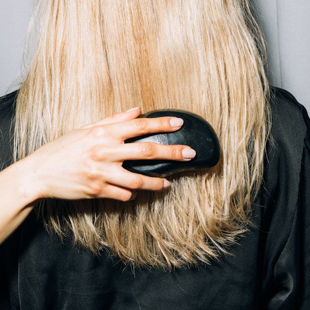 Stylist brushing smooth blonde hair at Tru Hair Studio in Brighton, CO, providing women’s hairstyling and maintenance services.