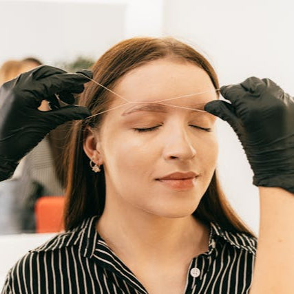 Woman receiving professional eyebrow threading at Tru Hair Studio in Brighton, Colorado, for precise brow shaping.