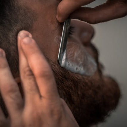 Barber giving a precise straight razor shave with hot lather at Tru Hair Studio in Brighton, CO, offering traditional barbering services.